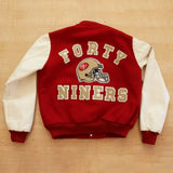 Red and white varsity jacket with 'Forty Niners' text and helmet logo on a wooden surface