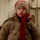 Child wearing a winter coat, red scarf, and patterned hat indoors.