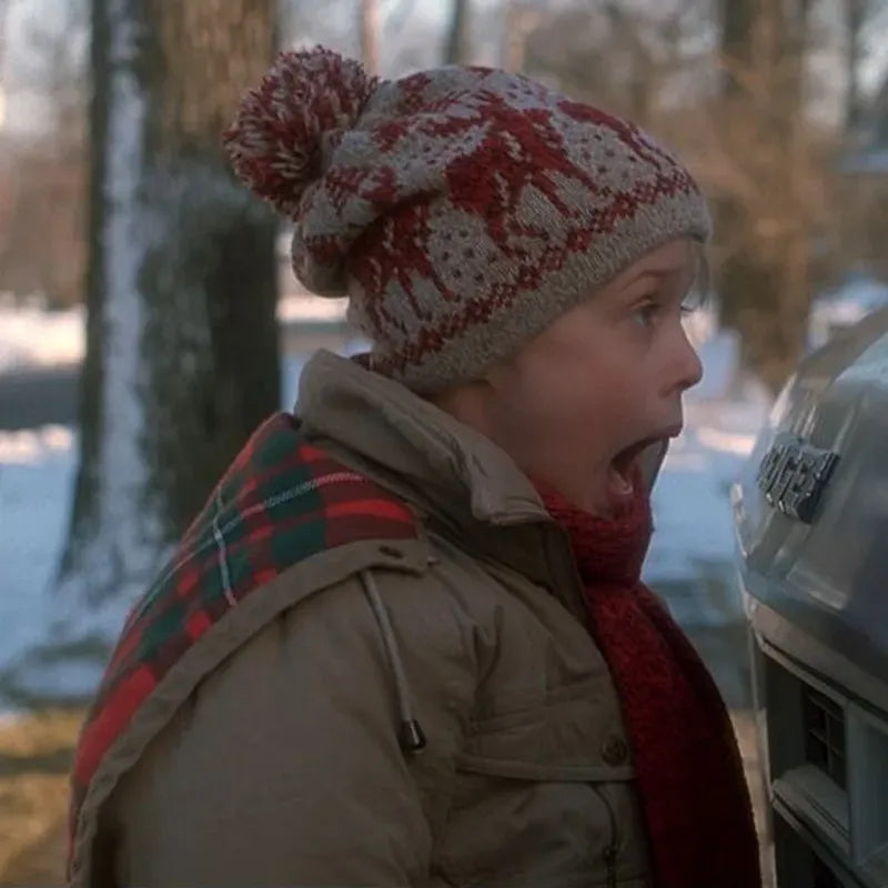 Person wearing a patterned knit hat and plaid scarf in a snowy outdoor setting