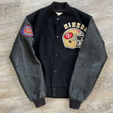 Black varsity jacket with sports team logos on a wooden surface