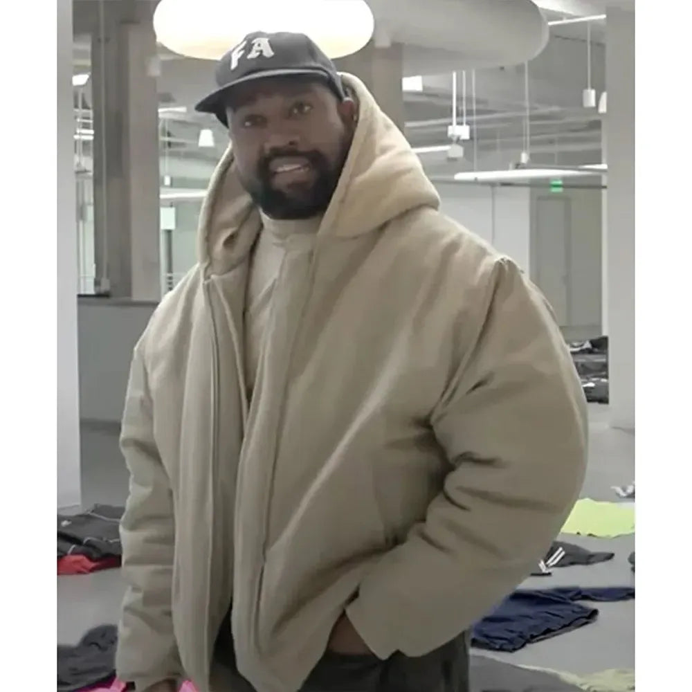 Man wearing a beige hoodie and black cap with 'FA' logo indoors.